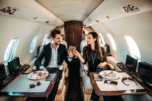 Un homme et une femme sont vus assis dans un jet privé, tirant des cours de champagne avec de la nourriture devant eux,