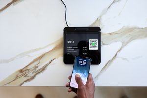 Main coupée d'un client tapant sur un smartphone sur un système de point de vente (POS) dans un café
