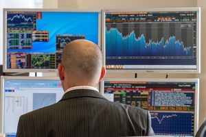 Un homme est assis, dos à la caméra, à un bureau doté de quatre écrans d'ordinateur affichant divers graphiques.