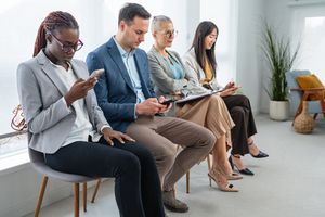 Quatre individus assis sur des chaises alignées, chacun manipulant des appareils électroniques ou des papiers