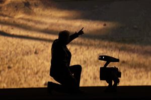 Silhouette d'une personne agenouillée et pointant du doigt une figure robotique à proximité devant un fond de désert