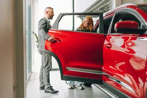 Femme faisant du shopping chez le concessionnaire, regardant une nouvelle voiture rouge avec un représentant commercial masculin